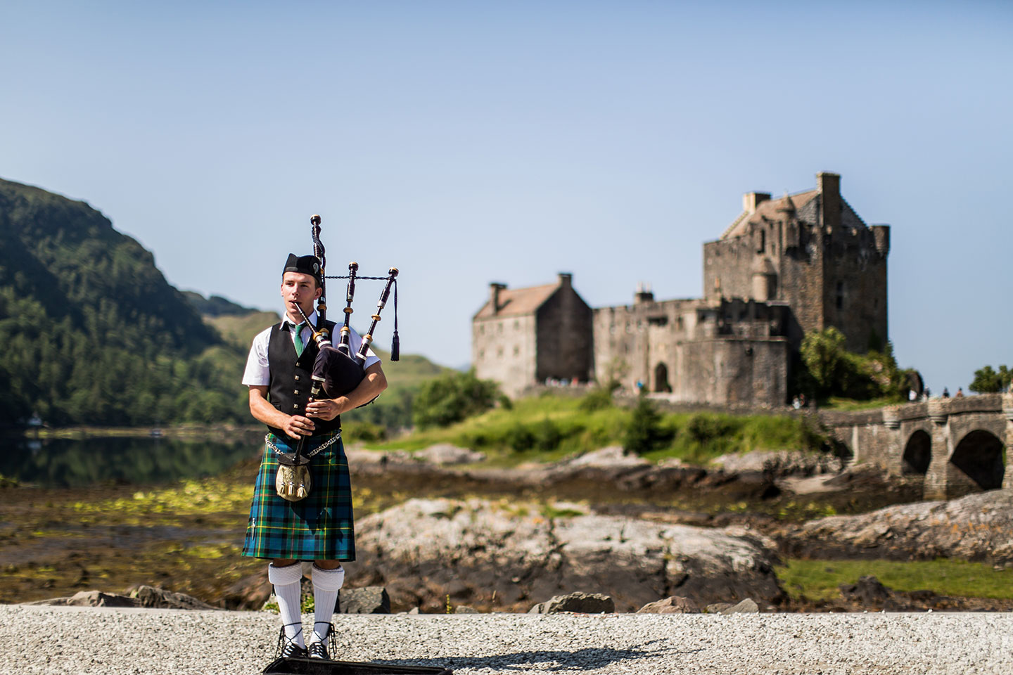 Bagpipe player in front of Eilean Donan Caslte in Scotland